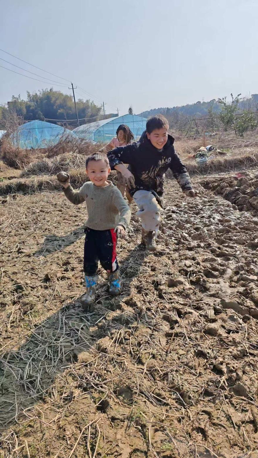 孩子和伙伴在泥田里奔跑嬉戏，举着泥块大笑