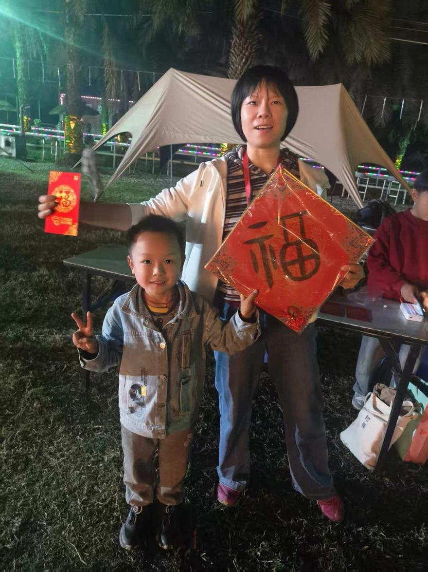 夜里的营地草坪上，孩子比着剪刀手，大人举着写好的福字